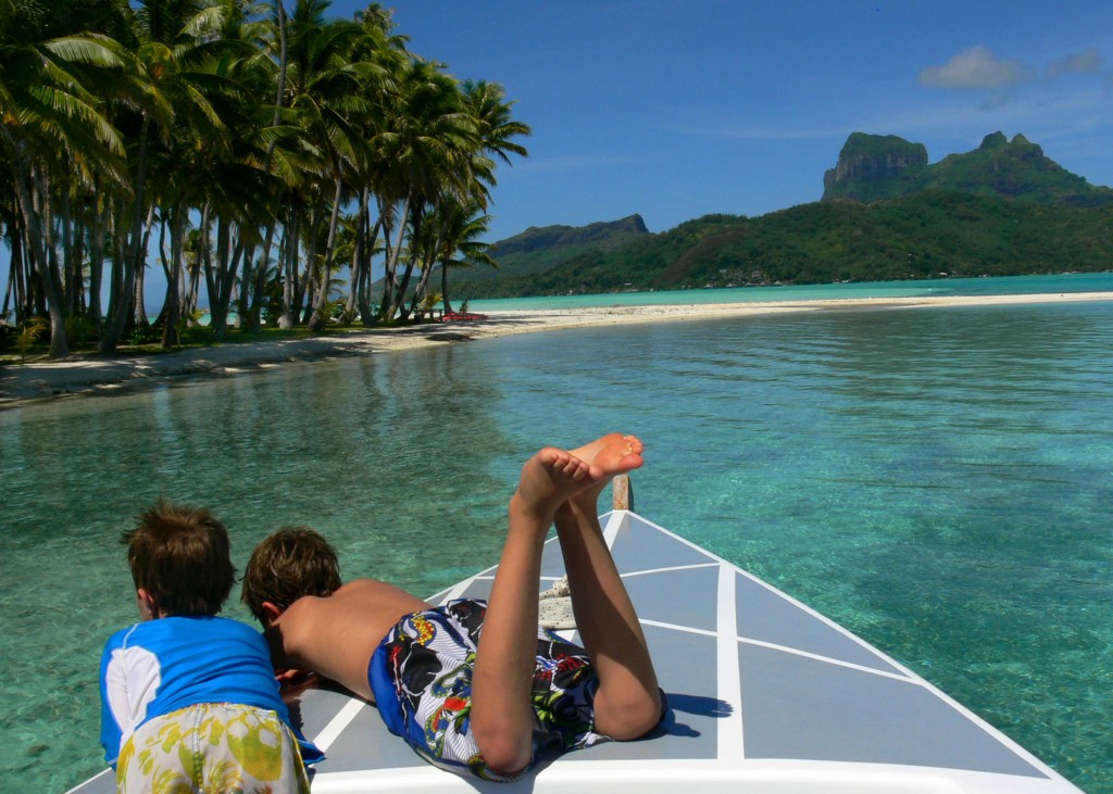 boys on boat on turquoise water with mountain island in background