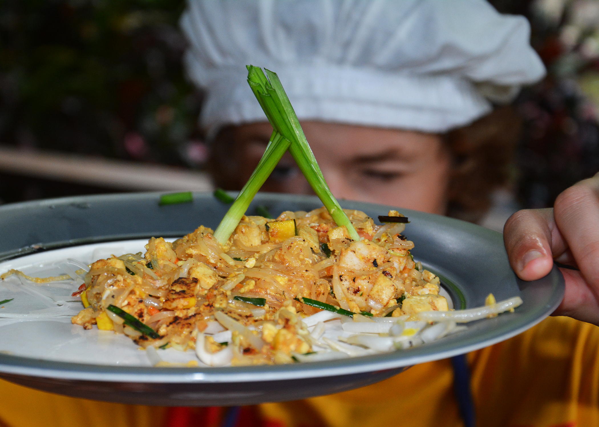 Boy in background holding a plate of Thai food in foreground