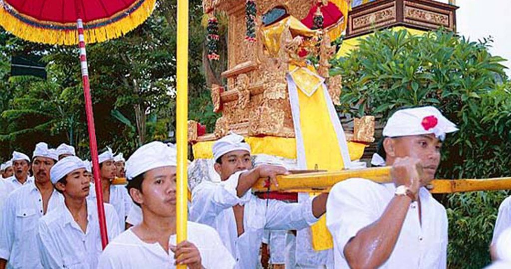 Man in traditional Hindu dress carrying temple instruments and umbrellas