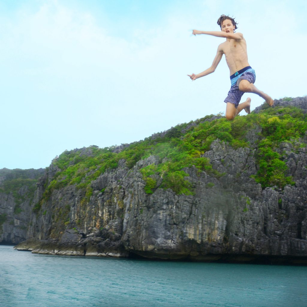 Boy jumping with turquoise water below and green cliffs in background
