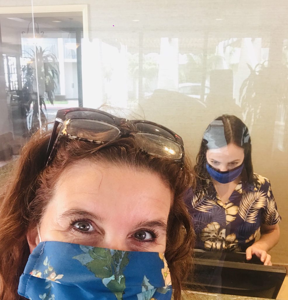 Woman with mask, plexiglass, receptionist with mask at hotel front desk